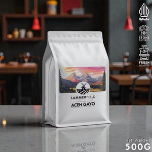 May include: A white coffee bag with a colorful mountain landscape label. The label features a windmill and the text "SUMMERFIELD ACEH GAYO". The bag also has the text "NET WEIGHT 500g". The bag is on a gray surface.