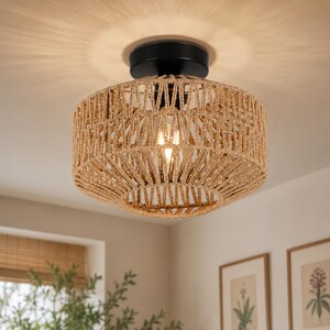 May include: A flush mount ceiling light fitting featuring a cylindrical shade crafted from woven natural tan rope. The fitting includes a black circular metal base that attaches to the ceiling, housing a single visible light bulb inside the shade.
