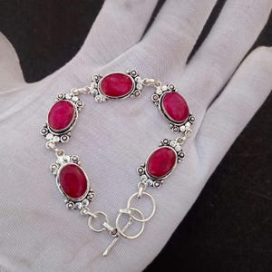 May include: Silver bracelet with six oval, deep red gemstones. The gemstones are set in ornate, oval frames connected by silver links. The bracelet has a toggle clasp. A piece of jewellery.