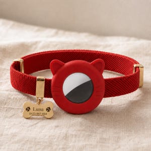 May include: A red fabric pet collar featuring a silicone cat-shaped holder for a tracking device. The collar includes a gold-toned metal bone-shaped tag engraved with the name Luna and the phone number 0123-987-654, along with gold-toned metal hardware.