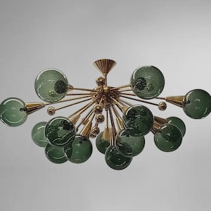 May include: A sputnik-style chandelier featuring a central gold-toned metal hub with numerous radiating arms. Each arm terminates in a spherical, textured green glass globe. The design includes smaller gold spheres interspersed among the arms.