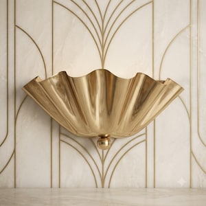 Può includere: Una lampada da parete con una struttura in metallo dorato lucido a forma di conchiglia, caratterizzata da un design ampio, smerlato e a ventaglio. L'apparecchio presenta un piccolo pomello sferico dorato alla base e una luce soffusa.