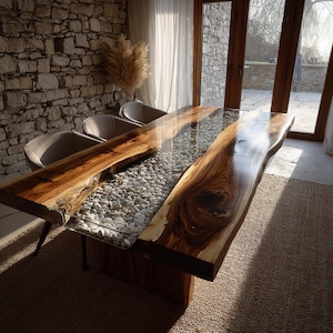 May include: A bespoke dining table featuring a live edge wooden top and a clear resin centre filled with white pebbles. The table has a natural wood grain finish and is supported by a wooden base. The table is approximately 244 cm long.