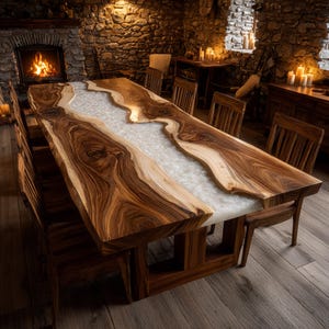 May include: A large, handcrafted wooden dining table with a unique design. The table features a live edge with a light-colored epoxy resin river running through the center. The wood has a rich, dark brown color with lighter streaks. The table is surrounded by matching wooden chairs.