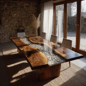 May include: A bespoke wooden dining table with a live edge. The table has a clear resin river filled with small, grey stones. It is supported by a solid wooden base and sits on a woven rug. The table's length is approximately 300 cm.