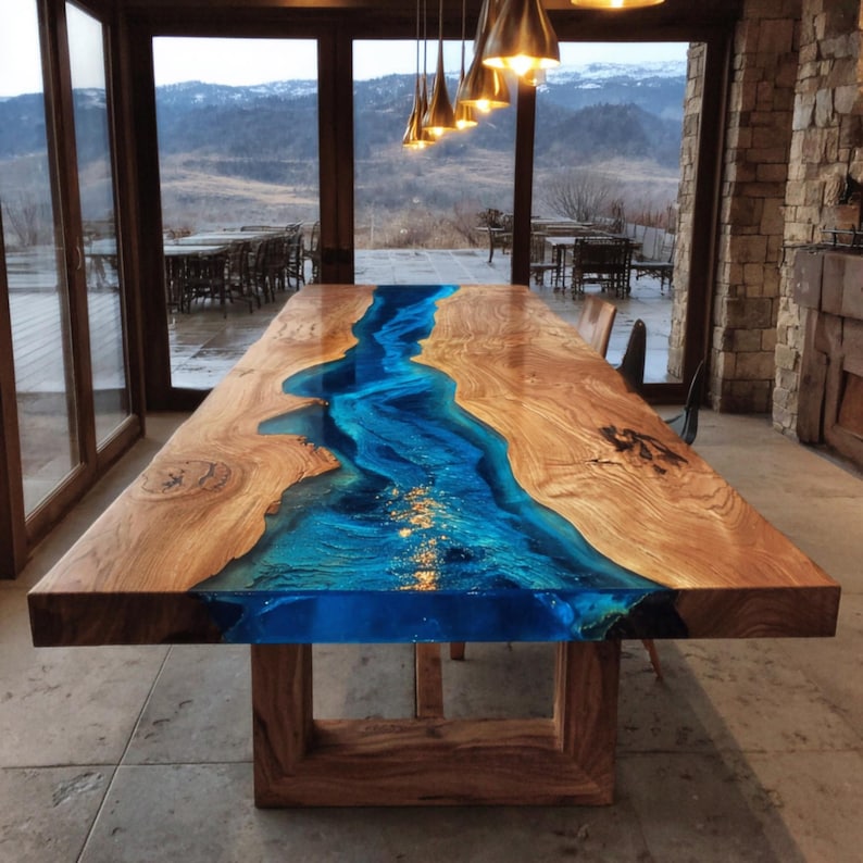 May include: A large wooden dining table with a blue resin river design. The table is rectangular, with a natural wood grain finish on the sides and a glossy blue center. The table is supported by a wooden base.