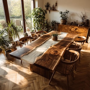 Op de afbeelding: Een grote, handgemaakte houten eettafel met een live edge design. De tafel heeft een lichtgekleurd epoxyhars middenstuk en is omringd door houten stoelen. De kamer heeft grote ramen en is gevuld met natuurlijk licht, wat een warme sfeer cre&euml;ert.