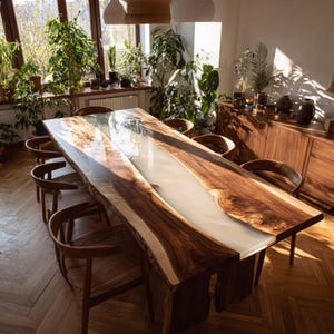 Op de afbeelding: Een grote, handgemaakte houten eettafel met een witte harsrivier in het midden. De tafel is omringd door houten stoelen. De kamer heeft een natuurlijke uitstraling, met zonlicht dat binnenvalt door een raam vol planten.