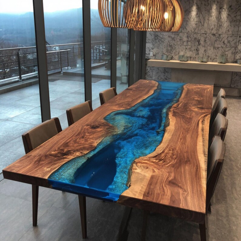 May include: A large, rectangular wooden dining table with a blue resin river design. The table is surrounded by eight chairs with brown upholstery. The table is made of natural wood with a glossy finish. The room has large windows and a modern chandelier.