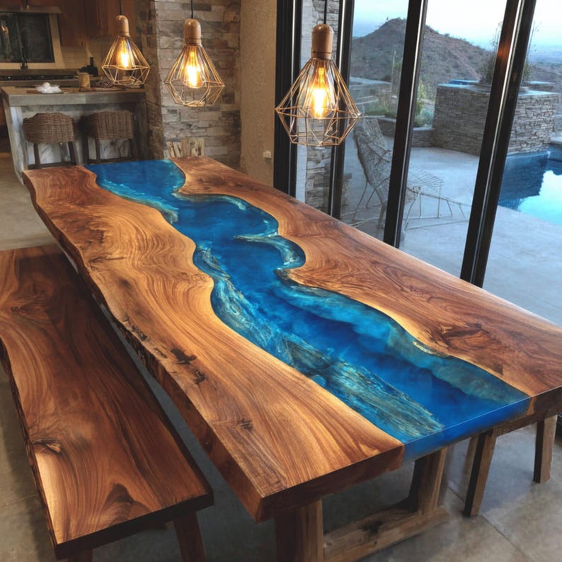 May include: A large, wooden dining table with a blue epoxy resin river running down the center. The table is paired with a matching wooden bench. The wood has a natural grain and is finished with a glossy coating. The table is approximately 10 feet long.