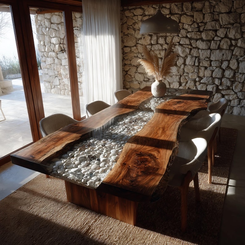 May include: A bespoke wooden dining table with a live edge design. The table has a central river of white stones set in clear resin. White chairs surround the table, which rests on a woven rug. The table measures approximately 300 cm in length.