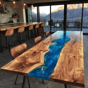 May include: A large, rectangular wooden dining table with a vibrant blue resin river running through the center. The table has a natural wood grain finish and is supported by black metal legs. The table is surrounded by brown leather chairs.