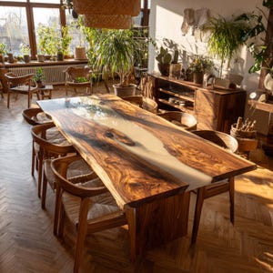 Op de afbeelding: Een grote, handgemaakte houten eettafel met een lichtgekleurde harsrivier in het midden. De tafel wordt omringd door houten stoelen met geweven zittingen. De kamer is gevuld met natuurlijk licht en planten, wat een warme sfeer cre&euml;ert.
