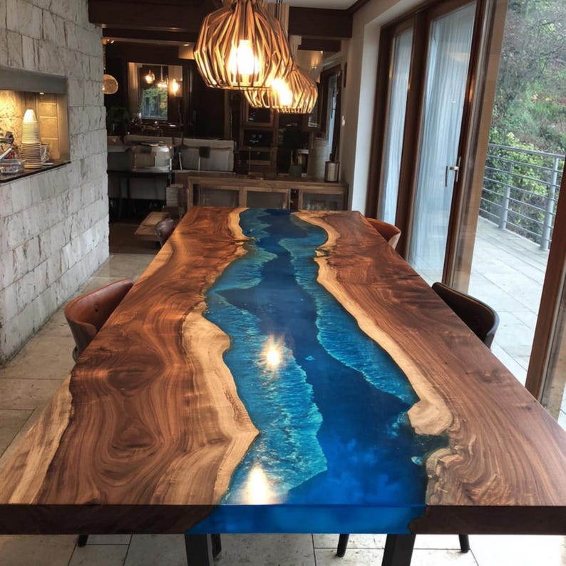 May include: A large, rectangular dining table with a unique design. The table features a dark brown wooden frame with a vibrant blue resin river running through the center. The table is illuminated by hanging lights.