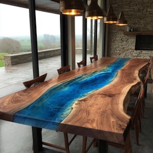 May include: A large, custom-made dining table with a unique design. The table features a live-edge wooden surface with a vibrant blue epoxy resin river running through the center. The table is supported by black metal legs and surrounded by wooden chairs.