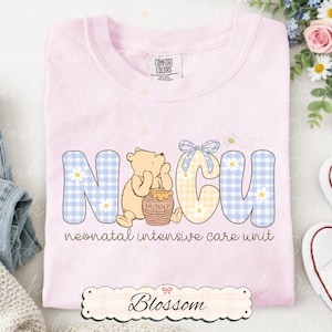 Peut inclure: Un t-shirt rose clair avec les lettres "NICU" dans un motif vichy bleu et jaune, représentant un ours de dessin animé avec un pot de miel. Les mots "neonatal intensive care unit" sont imprimés en dessous. L'étiquette de la marque indique "Comfort Colors".