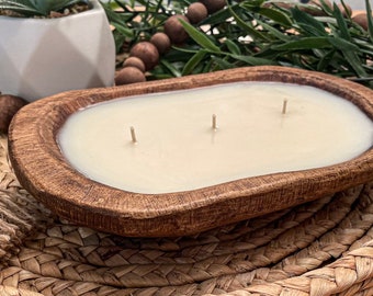 May include: A wooden bowl candle with three wicks and a white wax fill. The candle is sitting on a woven wicker surface.