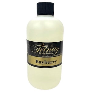 May include: A clear glass bottle with a black cap, filled with a light yellow liquid. The label is black with gold lettering that reads "Trinity candle factory premium scented candles Bayberry".