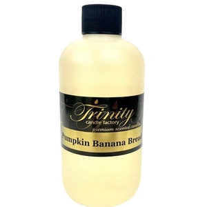 May include: A clear glass bottle with a black lid, filled with a light yellow liquid. The bottle has a black label with gold lettering that reads "Trinity candle factory premium scented candles Pumpkin Banana Bread".