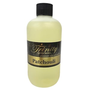 May include: A clear glass bottle with a black cap filled with a yellow liquid. The bottle has a black label with gold lettering that reads "Trinity Candle Factory Premium Scented Candles Patchouli".