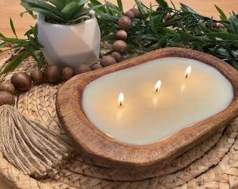 May include: A wooden bowl candle with three wicks burning. The candle is in a rustic wooden bowl and is surrounded by a woven mat and a garland of brown beads.