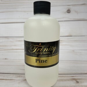 May include: A clear glass bottle with a black lid and a gold label that says "Trinity candle factory premium scented candles Pine".