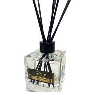 May include: A clear glass bottle with black reeds and a gold label that reads "Trinity Soy Factory Candles Pumpkin Banana Bread".