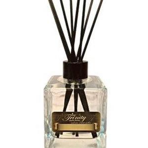 May include: A clear glass bottle with a black lid and black diffuser sticks. The bottle has a gold label with the text "Trinity" on it.