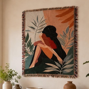 Pode incluir: Uma tapeçaria de parede retangular tecida com uma ilustração estilizada de uma figura sentada entre folhagens tropicais. O design incorpora uma paleta de preto, terracota, verde sálvia e creme, com uma borda decorativa de franjas.
