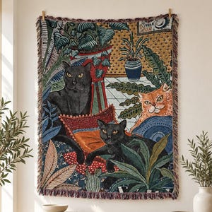 May include: A rectangular woven tapestry wall hanging featuring a vibrant scene of two black cats and one orange cat surrounded by lush green potted plants and foliage. The design includes intricate patterns, deep blue, red, and gold accents.
