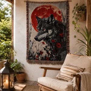 May include: A rectangular woven wall tapestry featuring a detailed illustration of a wolf in profile against a large, solid red moon. The wolf is rendered in shades of black and grey, surrounded by red flowers and tall grass, with fringed edges.