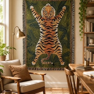 May include: A rectangular woven throw blanket featuring a large, centered tiger illustration with orange, black, and white fur against a dark olive green background filled with dark green tropical leaf patterns and a fringed edge on all sides.