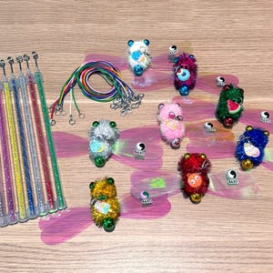May include: A set of cat toy wands with glittery handles, colorful cords with metal clips, and several fuzzy pom-pom creatures featuring googly eyes, small bells, and translucent pink wings. Each creature includes a small charm and a BAXO logo.