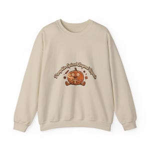 May include: A beige crewneck sweatshirt featuring a central graphic of an orange pumpkin character with swirling eyes holding a steaming mug. The text "Pumpkin Spiced Beyond Repair" is arched above the pumpkin, accompanied by small star and leaf icons.