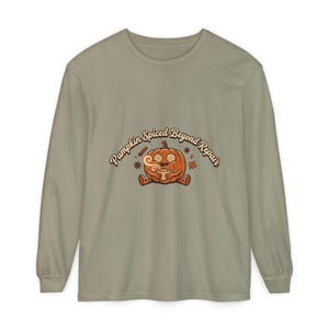 May include: A sage green long-sleeve shirt featuring a central graphic of a cartoon pumpkin with spiral eyes holding a steaming mug. The text above the pumpkin reads Pumpkin Spiced Beyond Repair, accompanied by small illustrations of cinnamon and leaves.