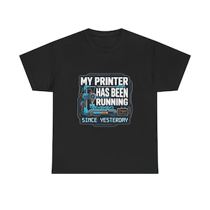 May include: A black short-sleeved t-shirt featuring a graphic print of a 3D printer with the text "MY PRINTER HAS BEEN RUNNING SINCE YESTERDAY" in white and blue. The design includes a small digital display showing "24H+" and a progress bar.