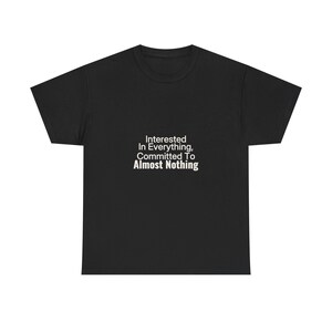 May include: A black short-sleeved t-shirt featuring white text centered on the chest that reads: Interested In Everything, Committed To Almost Nothing. The garment has a crew neckline and a standard fit with short sleeves and a straight hemline.
