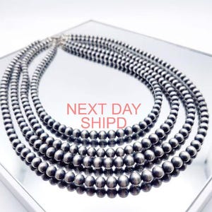 May include: A multi-strand necklace featuring polished silver-toned spherical beads arranged in concentric circles. The text NEXT DAY SHIPD is overlaid in the center of the necklace. The beads have a reflective metallic finish.