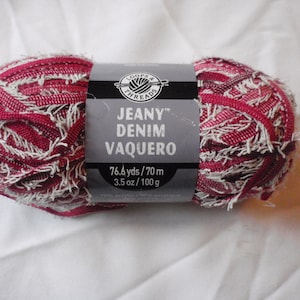 May include: A skein of Loops & Threads Jeany Denim Vaquero yarn in a red and white colorway. The label reads "Jeany Denim Vaquero" and "76.6 yds/70 m, 3.5 oz/100 g".