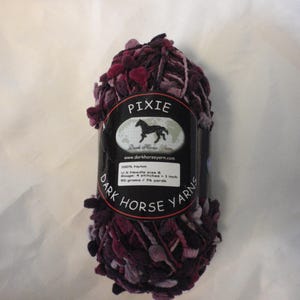 May include: A skein of Pixie Dark Horse Yarns in shades of deep purple, burgundy, and light lavender. The black label features a horse logo, 100% nylon content, U.S. needle size 8, a gauge of 4 stitches per inch, and 50 grams / 76 yards.