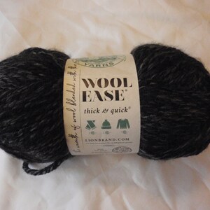 Peut inclure: Une pelote de laine Wool Ease noire et grise avec une étiquette blanche sur laquelle est inscrit "Wool Ease thick & quick" et "Lion Brand.com".
