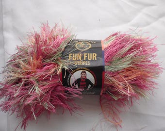 May include: A ball of Lion Brand Fun Fur Stripes yarn in pink, green, and orange hues. The yarn has a fluffy texture and is wrapped with a black and orange label that reads "Fun Fur Stripes".