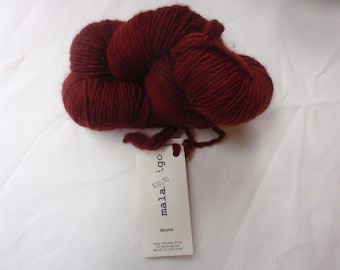 Puede incluir: Una madeja de hilo rojo oscuro con una etiqueta blanca que dice "mala.igo" y "10,50 €" con la palabra "worsted" debajo.