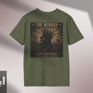 Pode incluir: Uma t-shirt verde-oliva com um gráfico quadrado escuro nas costas. A estampa retrata uma figura carregando um grande feixe de espadas, com o texto THE BURDEN, CARRY THE WEIGHT e SOME LOADS NEVER LEAVE YOU em uma fonte com aspecto desgastado.
