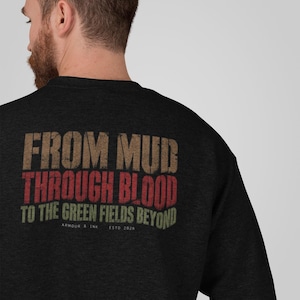 May include: A charcoal grey crewneck sweatshirt featuring a distressed graphic on the back. The text reads FROM MUD, THROUGH BLOOD, TO THE GREEN FIELDS BEYOND, with ARMOUR & INK ESTD 2025 printed in smaller white lettering underneath the main design.