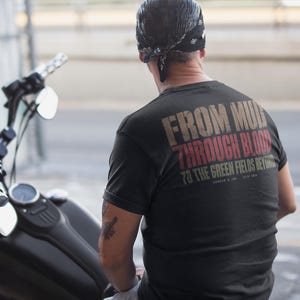 Peut inclure: Un t-shirt noir à manches courtes avec l'inscription FROM MUD THROUGH BLOOD TO THE GREEN FIELDS BEYOND imprimée au dos en lettres usées beige, rouge et vert, avec le petit texte ARMOUR & INK ESTD 1999 sous le graphisme principal.