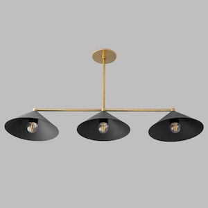 A linear chandelier featuring a horizontal brass rod suspended from a matching circular ceiling canopy. Three matte black conical shades are attached to the rod, each housing a single exposed light bulb in the centre of the shade.