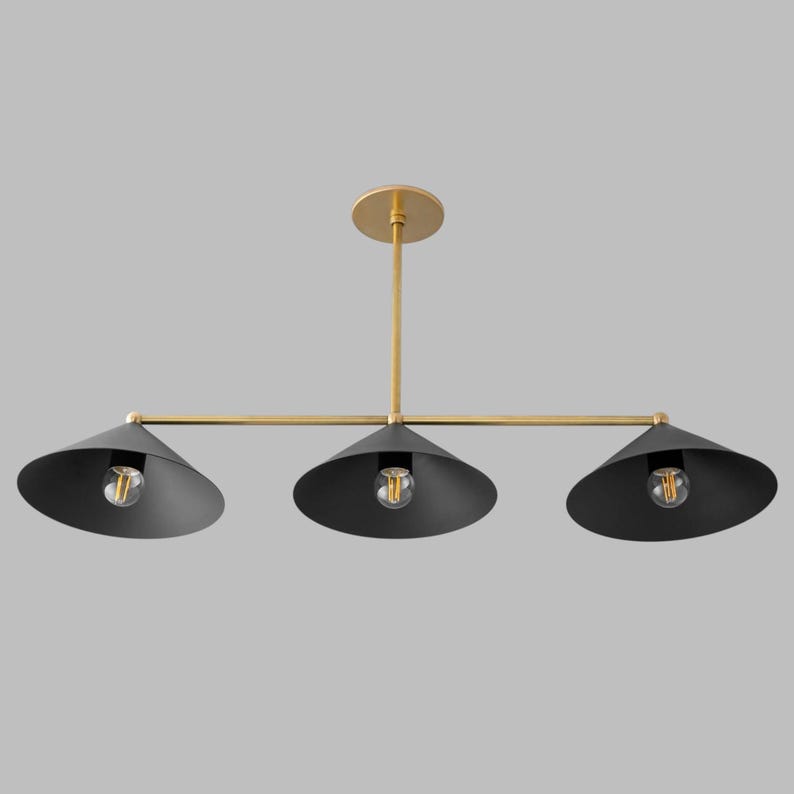 A linear chandelier featuring a horizontal brass rod suspended from a matching circular ceiling canopy. Three matte black conical shades are attached to the rod, each housing a single exposed light bulb in the centre of the shade.