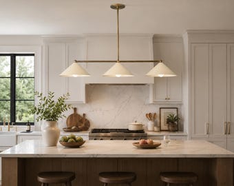 May include: A linear pendant light fixture featuring three off-white conical shades suspended from a central brass-toned horizontal bar and a single vertical rod attached to a circular ceiling canopy, providing downward illumination over a kitchen island.