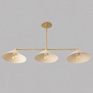 A three-light linear chandelier featuring a central brass rod and a horizontal bar supporting three cone-shaped shades in a matte cream finish. Each shade houses a single exposed light bulb, creating a balanced and symmetrical fixture.
